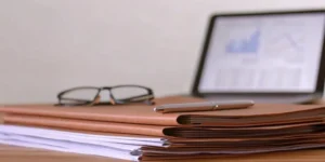 FDA submission documents, pen, and glasses on a desk. Laptop with charts open in the background.