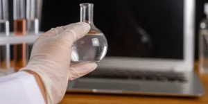 Gloved hand with a lab flask and laptop, ensuring data integrity with ALCOA+ principles.