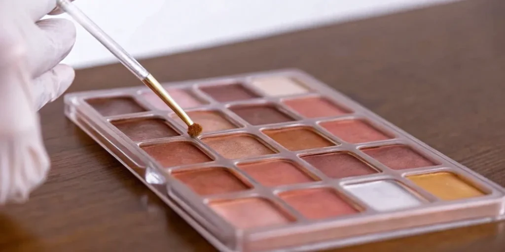 Gloved hand with a brush on a makeup palette, following an allergen control plan.