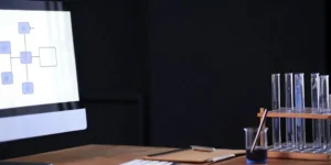Computer, lab notebook, and test tubes on a desk for a GLP training course.