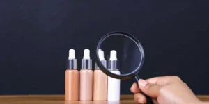 A person performs quality risk management by inspecting cosmetic bottles with a magnifying glass.