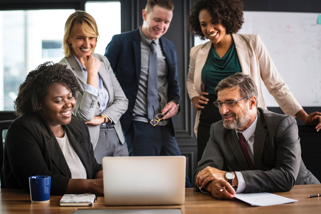 Diverse professionals smiling around laptop in office