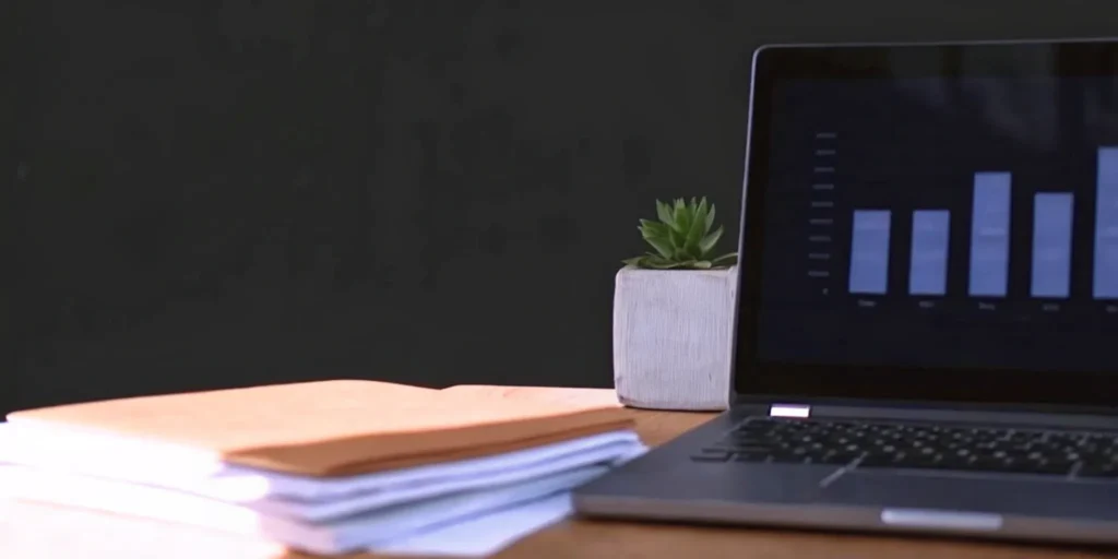 Laptop displaying bar chart with plant and folders
